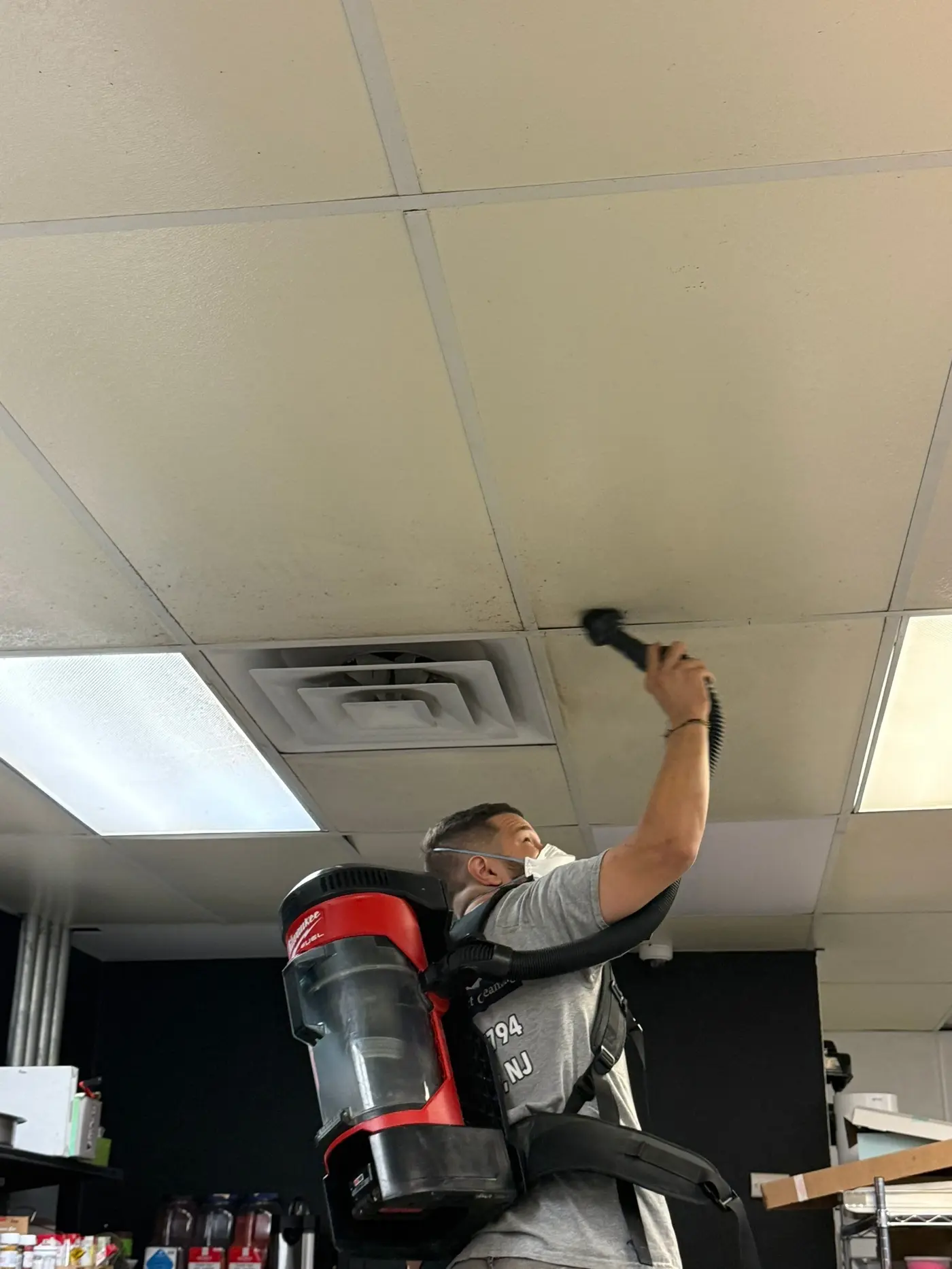 A technician vacuuming a ceiling vent during an air duct cleaning service